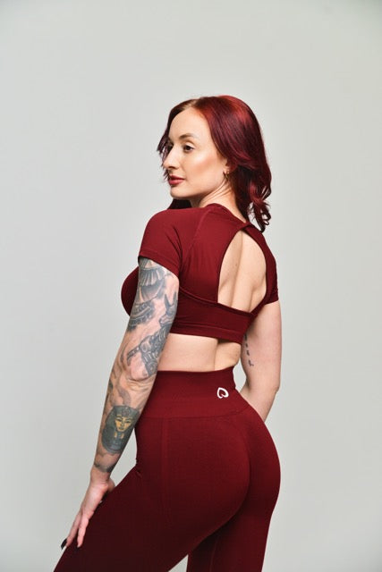 woman standing facing to the side and back wearing red activewear cropped top